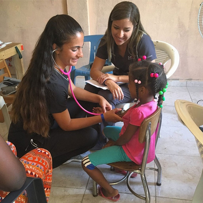 UMHS students (left to right) Paola Mora & Ariana Hernandez examine a young patient in La Caleta, Boca Chica, Dominican Republic. Photo: UMHS Med4You